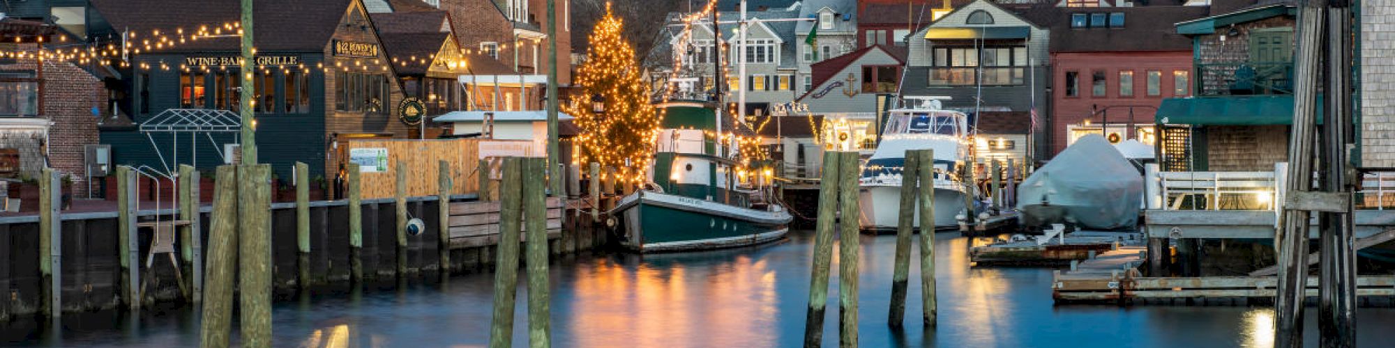 A picturesque harbor scene with boats, decorated buildings, and a church steeple in the background during twilight.