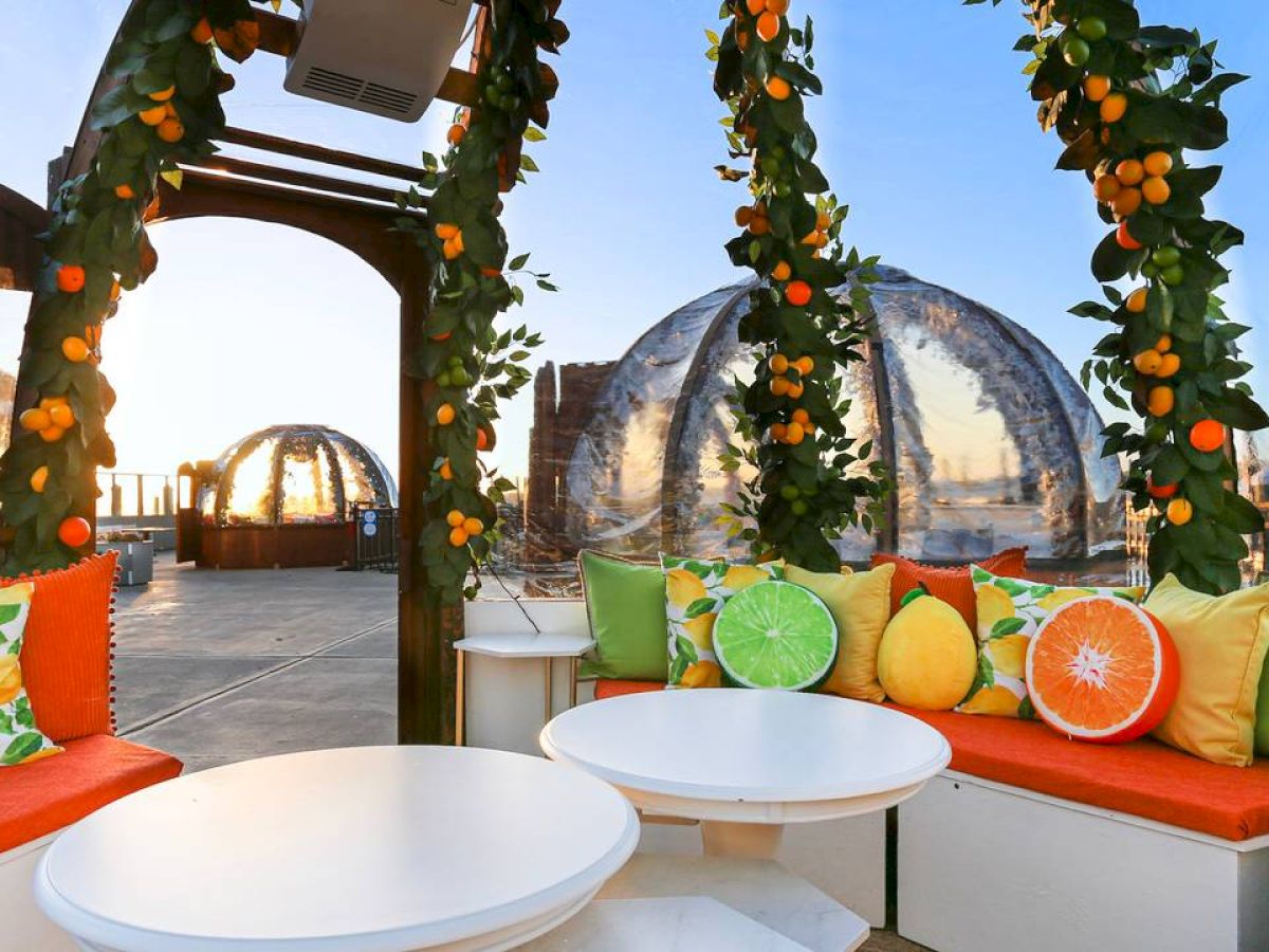 Outdoor seating with colorful fruit-themed cushions, surrounded by plants and clear igloos in the background at sunset.