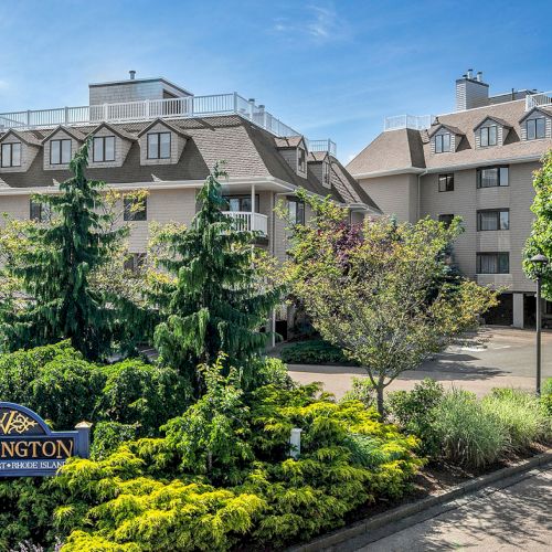 The image shows a residential building complex with well-maintained landscaping and a sign reading 