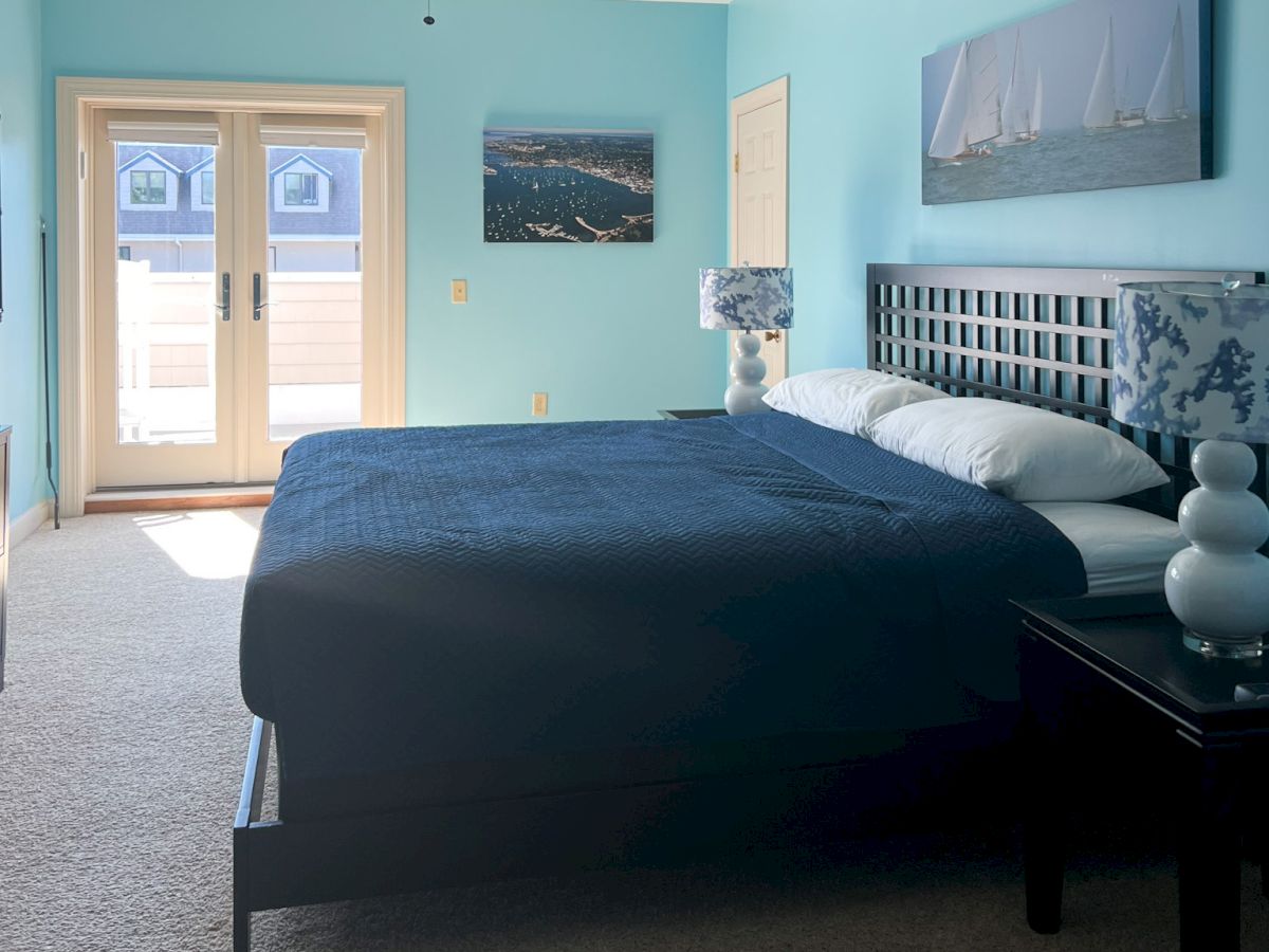 A bedroom with a large bed, blue walls, nautical-themed decor, and doors leading to a balcony. White-and-blue lamps are on side tables.