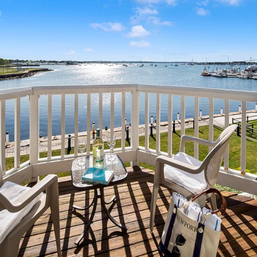 A balcony view with two chairs, a table with drinks, and a book overlooking a sunny waterfront and marina.