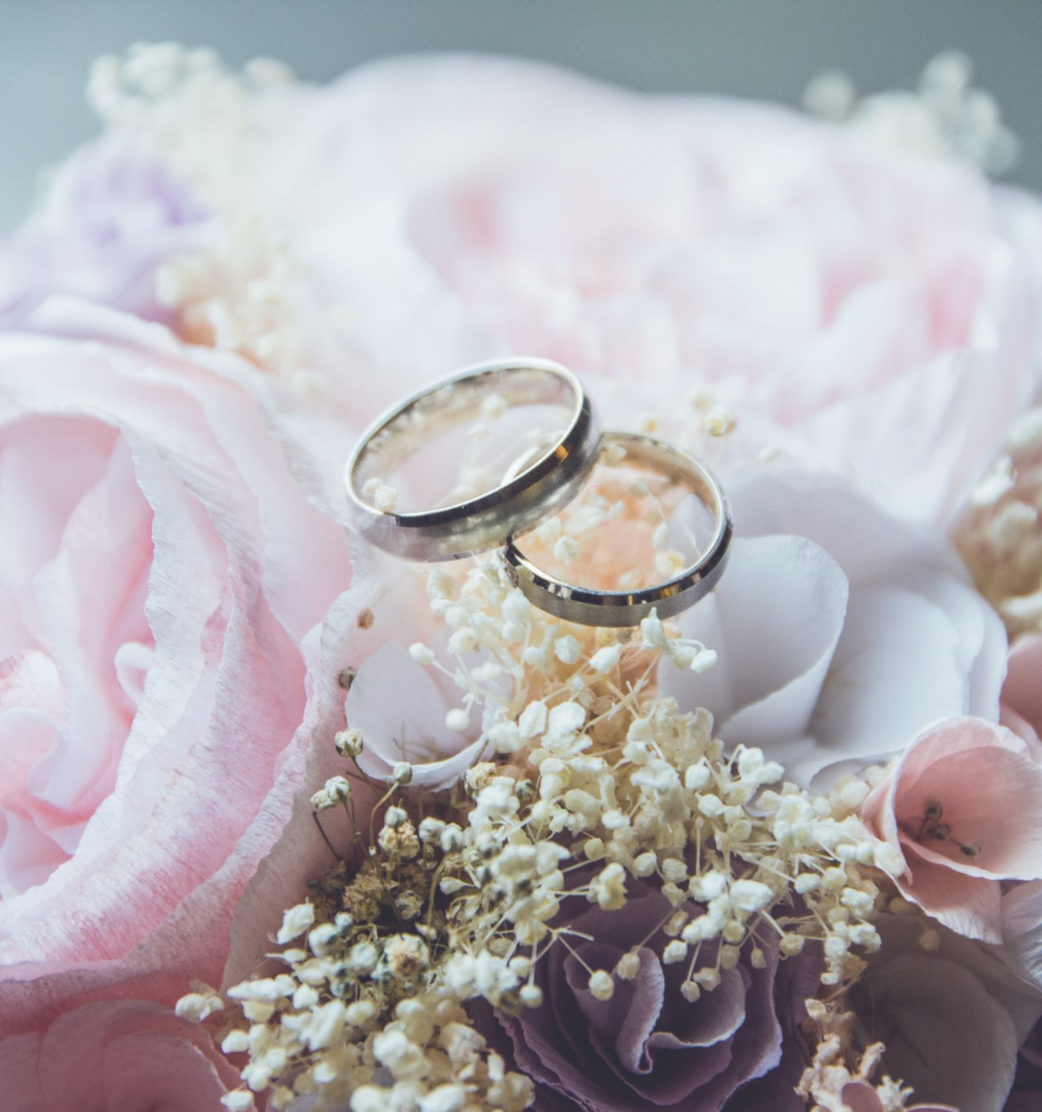 A pair of wedding rings is resting on a bouquet of pink and white flowers with delicate greenery.