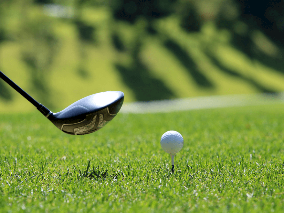 A golf club is about to hit a golf ball on a tee, set against a grassy golf course background.