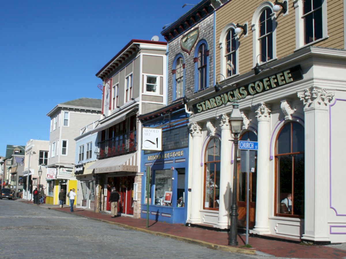 A streetscape with colorful buildings, including a Starbucks Coffee, lines a cobblestone street under a clear blue sky.