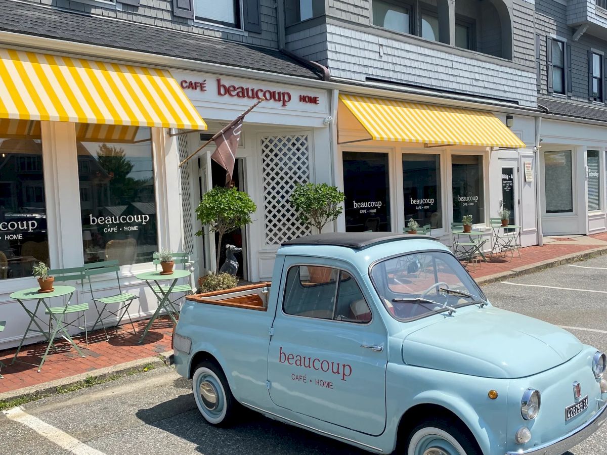 A light blue vintage car parked in front of a building with yellow-striped awnings and outdoor seating.