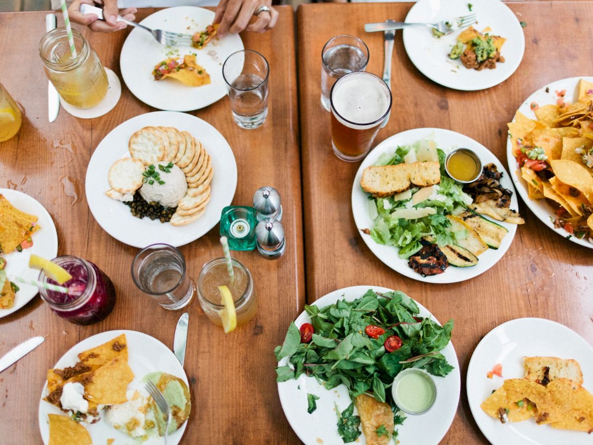 A table with various dishes including salads, nachos, and bread, along with drinks, viewed from above.