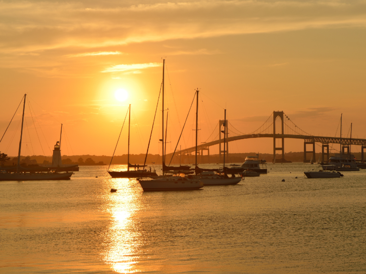 Sailboats on the water at sunset with a bridge in the background, creating a peaceful and scenic view.