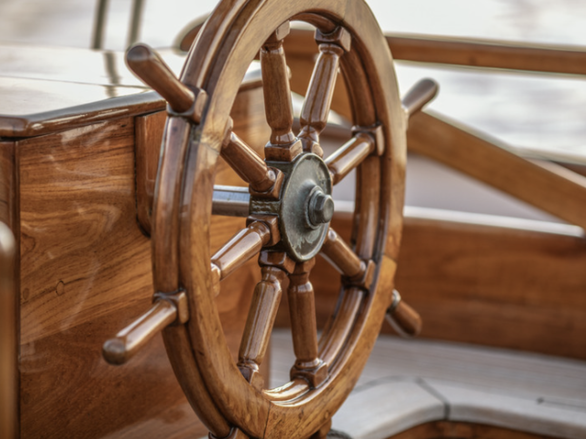 The image shows a wooden ship's wheel attached to a wooden helm station, used for steering boats.