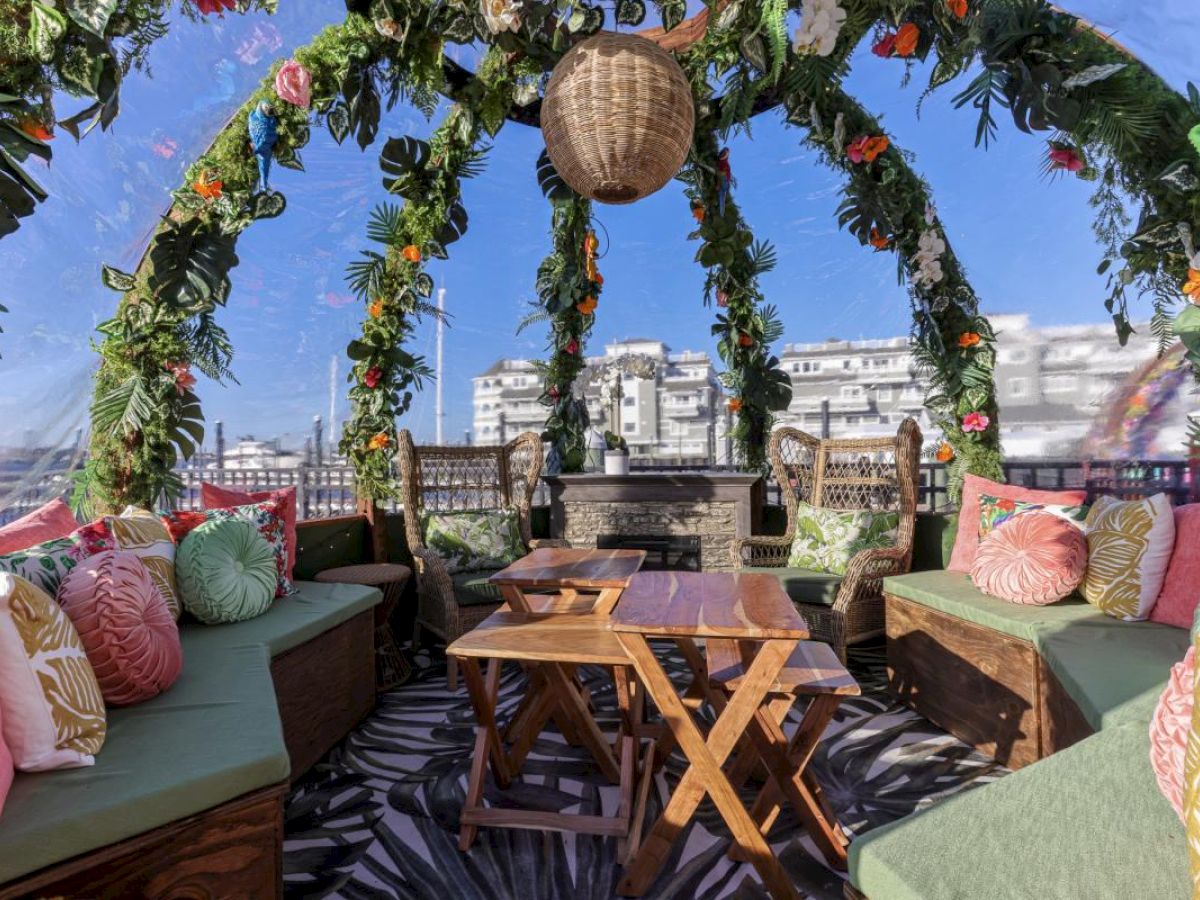 A cozy, tropical-themed outdoor seating area with cushions, plants, and views of the city through a clear dome.