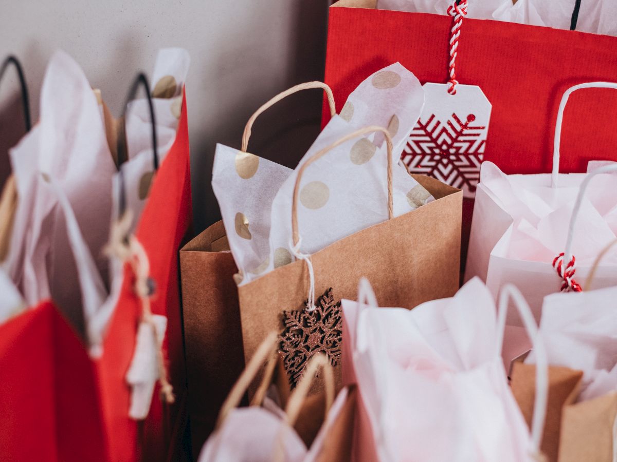 The image shows various gift bags filled with decorative tissue paper, featuring holiday themes in red, brown, and white colors.