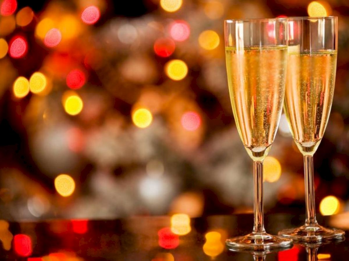 Two champagne flutes with bubbly liquid, set against a festive background of blurred colorful lights.