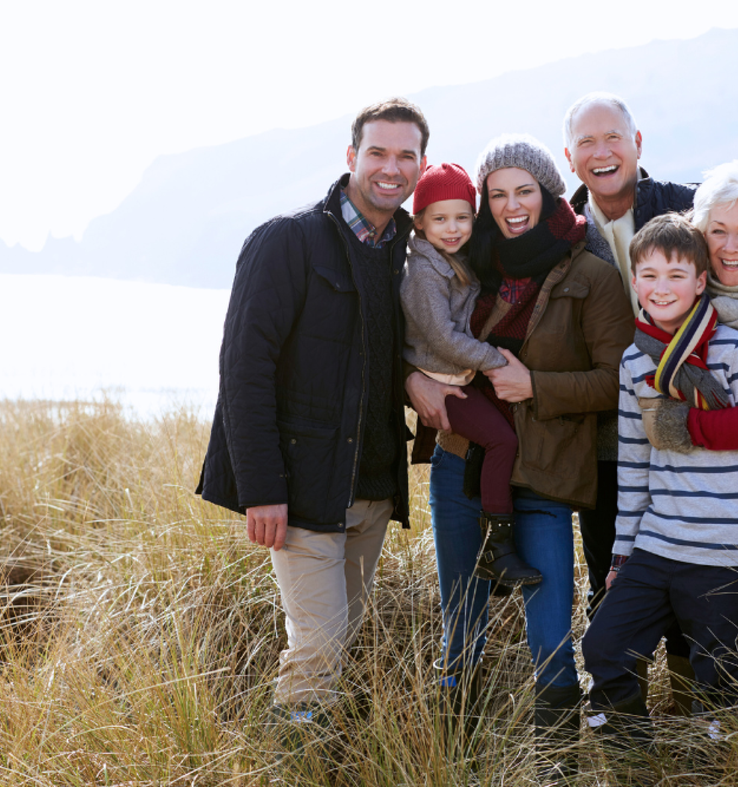 A family of six smiling and posing in a grassy, coastal landscape.